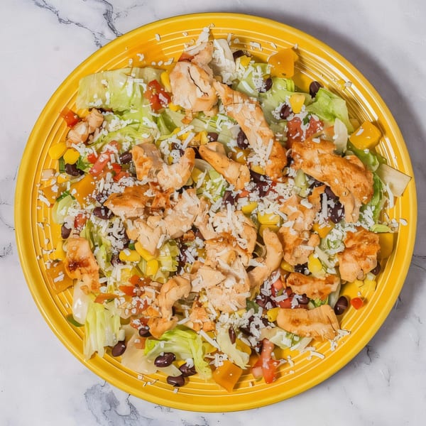 Serranos Mexican Grill's chicken salad with lettuce, corn, black beans, tomatoes, and cheese on a yellow plate.