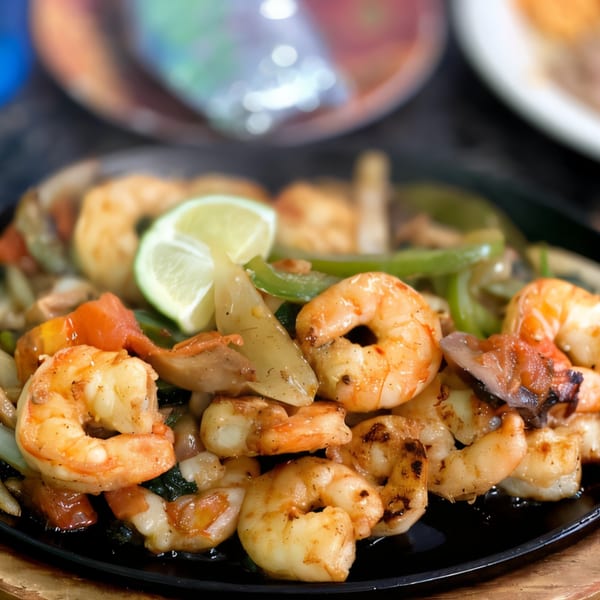 Sizzling shrimp fajitas with bell peppers, onions, and a lime wedge on a black skillet.