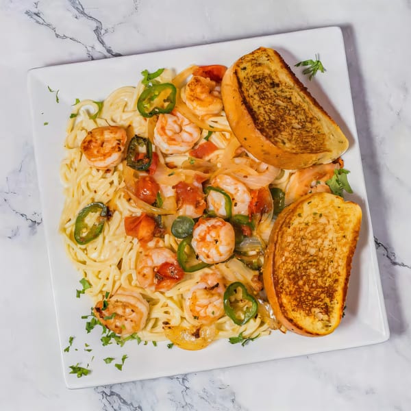 Shrimp pasta with jalapeños, onions, tomatoes, and two slices of garlic bread on a white plate.